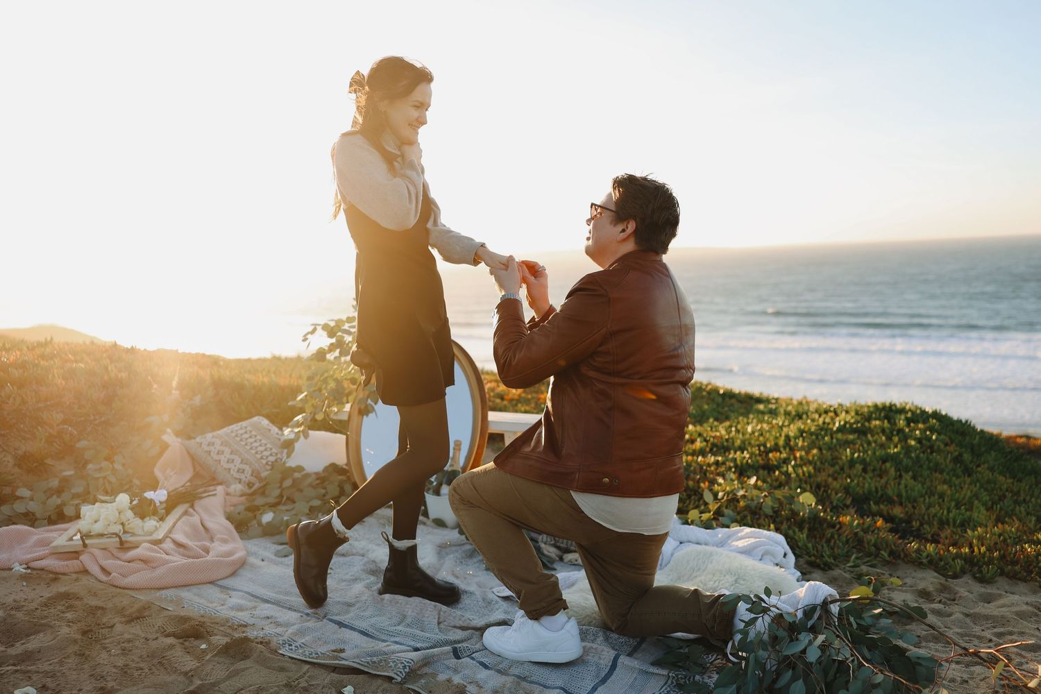 An intimate marriage proposal moment on a coastal cliff during golden hour.