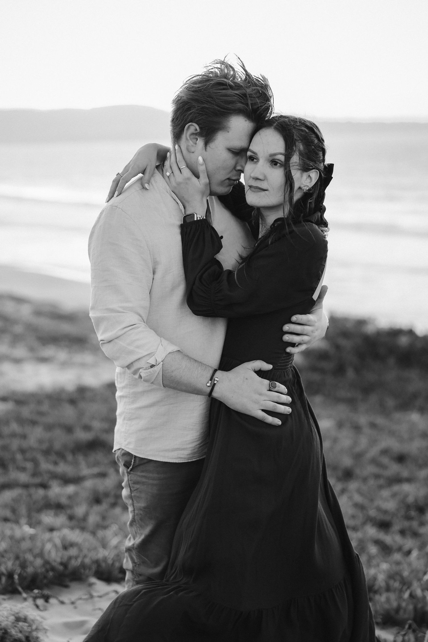 A black and white portrait of a couple in an intimate embrace on coastal cliffs.
