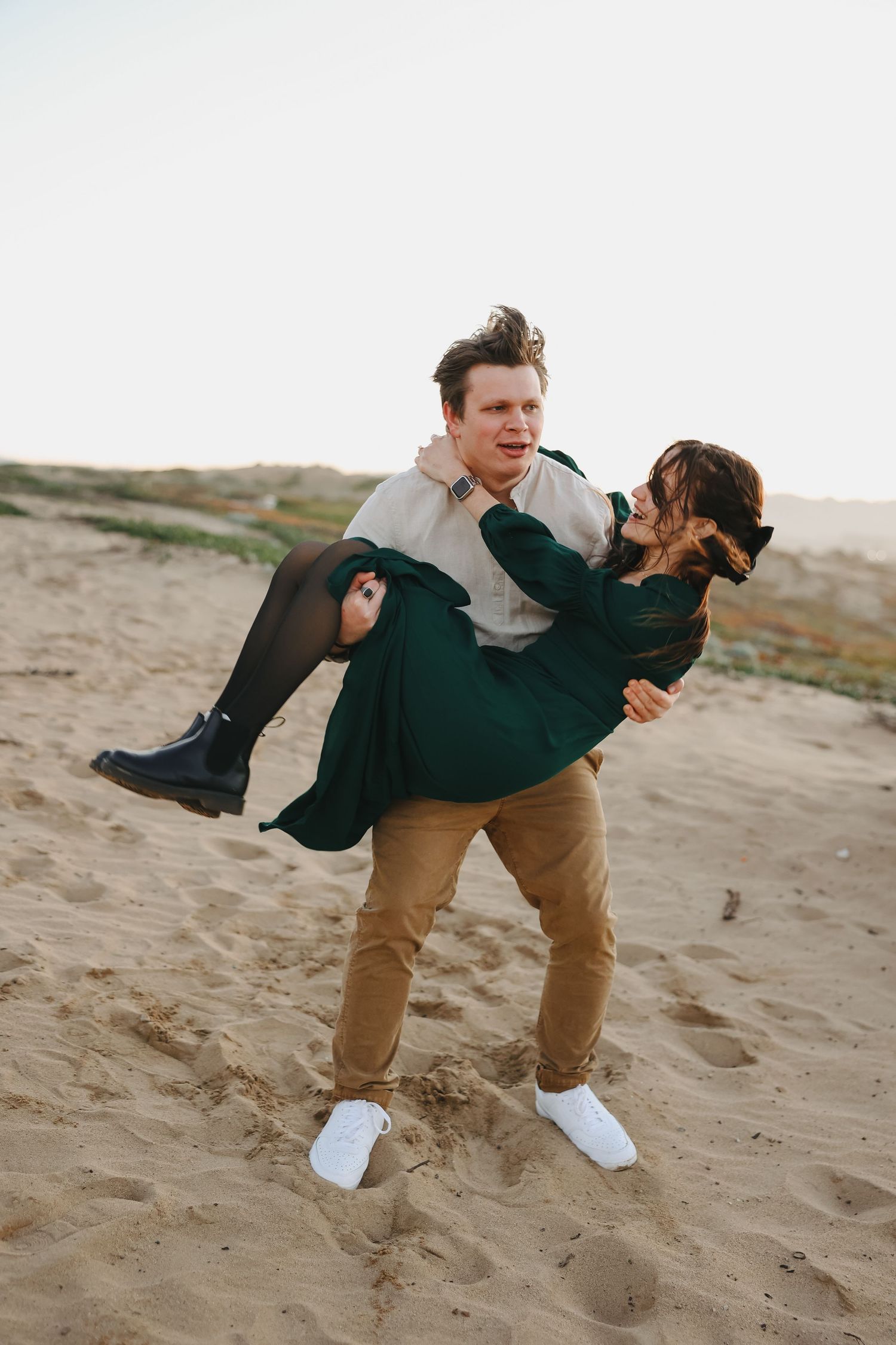 A playful moment as one person carries another across a beach near the ocean.