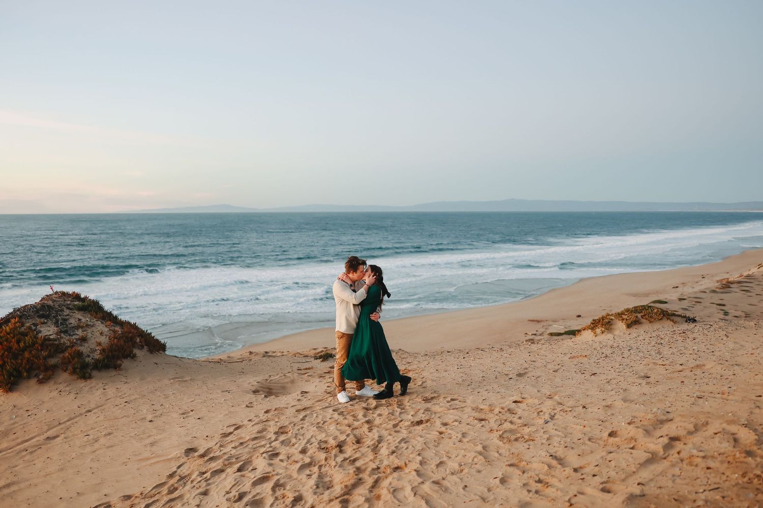 Romantic couple in evening light sharing an intimate dance moment on a secluded beach with crashing waves.