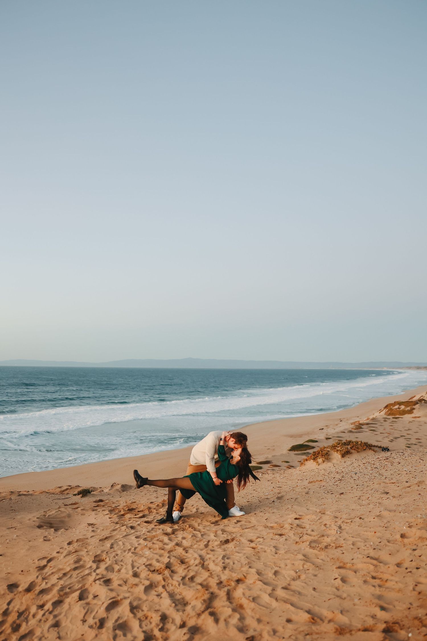 Romantic beach photoshoot features elegant dance pose against coastal backdrop.