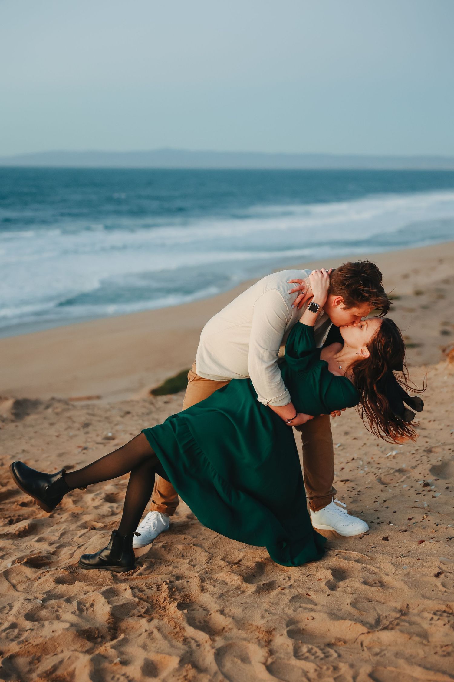 Dramatic dance pose captured on beach with emerald dress contrasting against sandy shore.