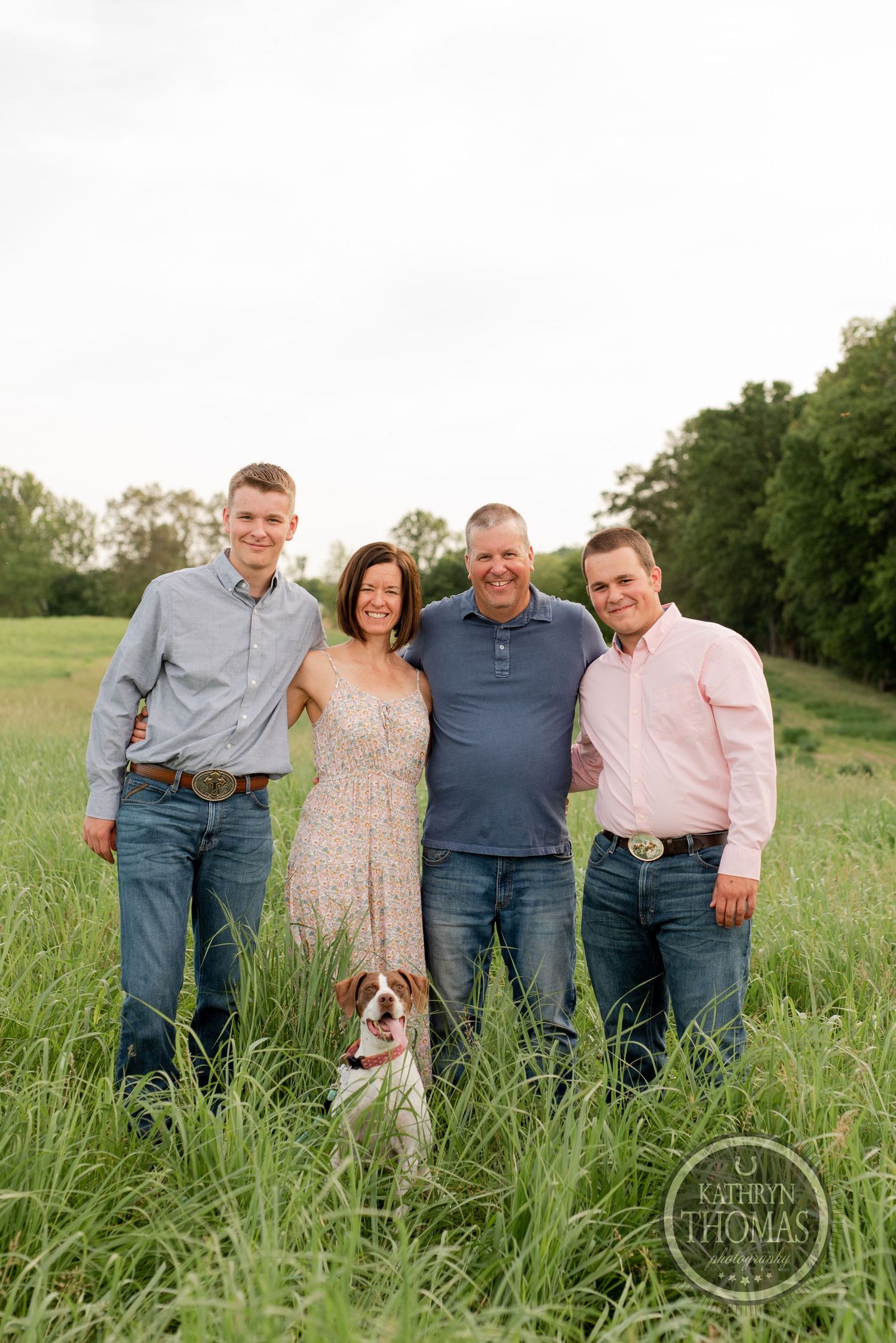Family portrait with small dog in grassy field during sunset.