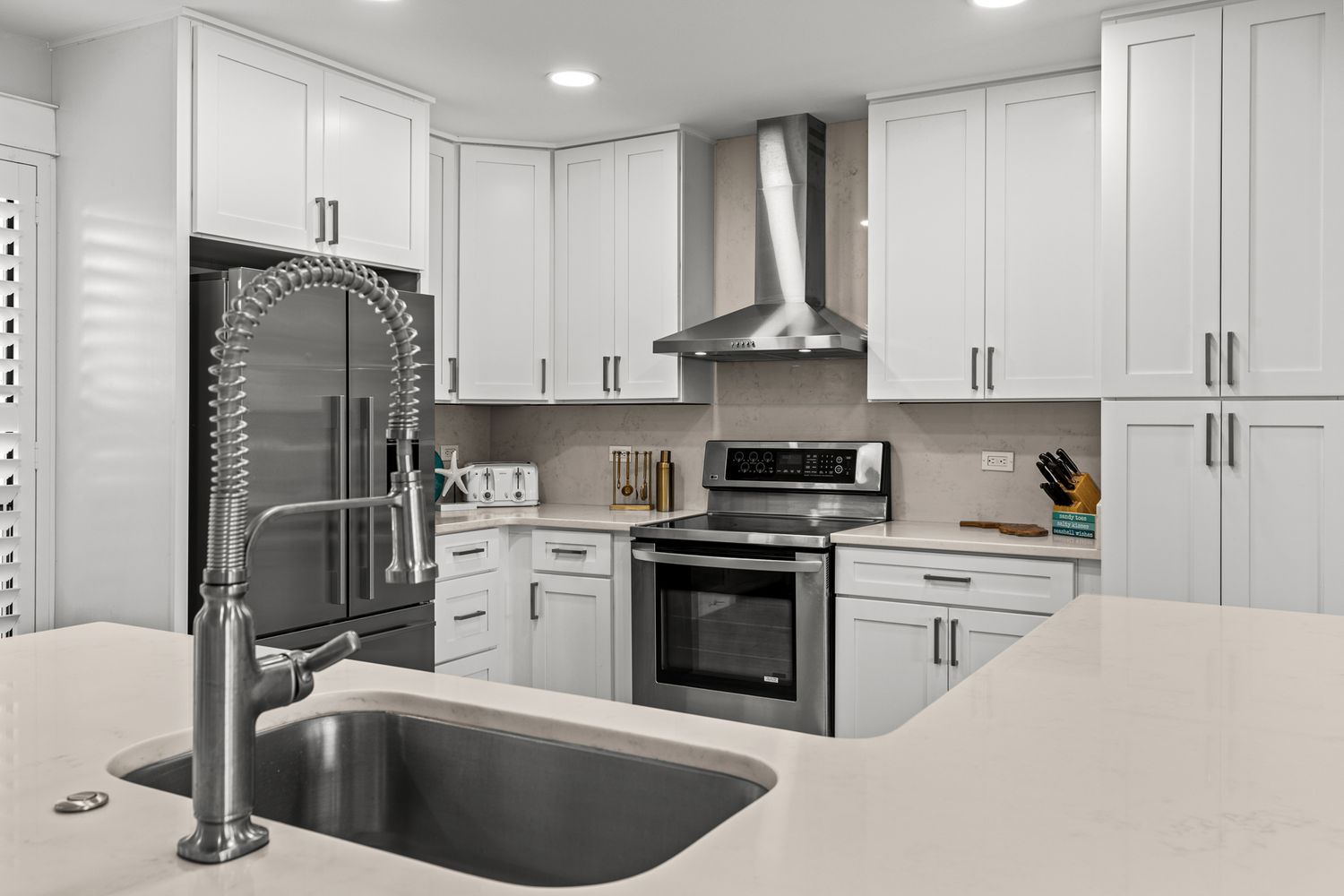 Modern white kitchen with stainless steel appliances, pull-down faucet, and quartz countertops.