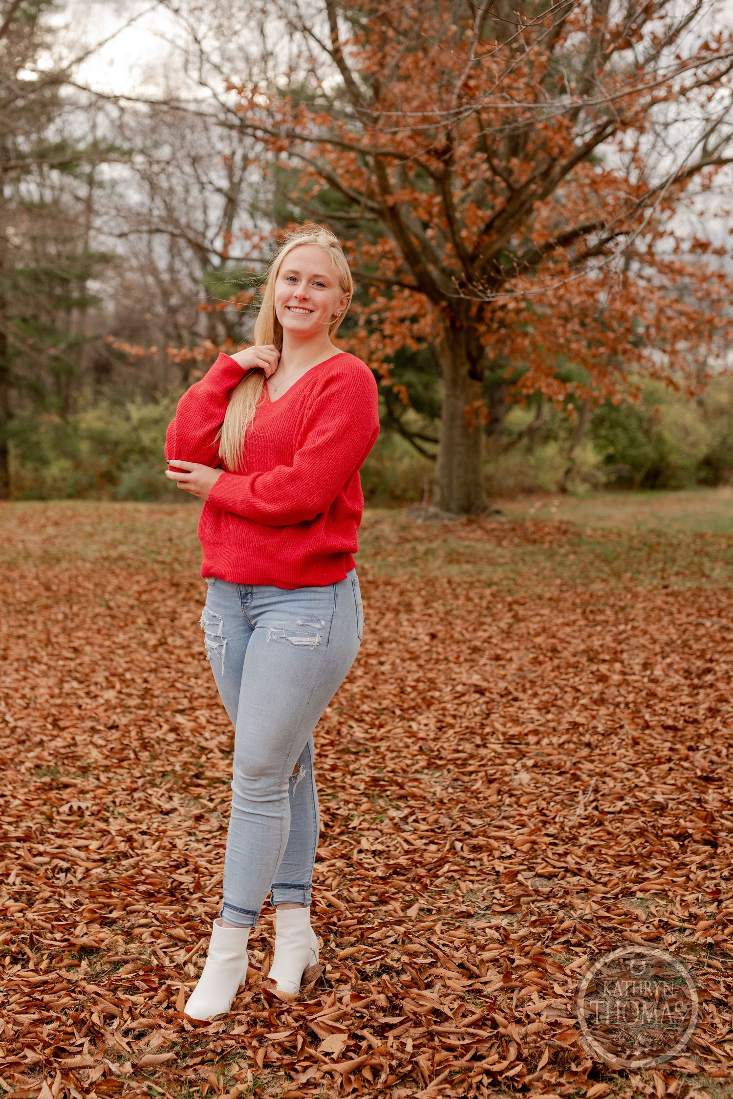 Casual autumn fashion portrait featuring bright red sweater and light denim in fallen leaves.