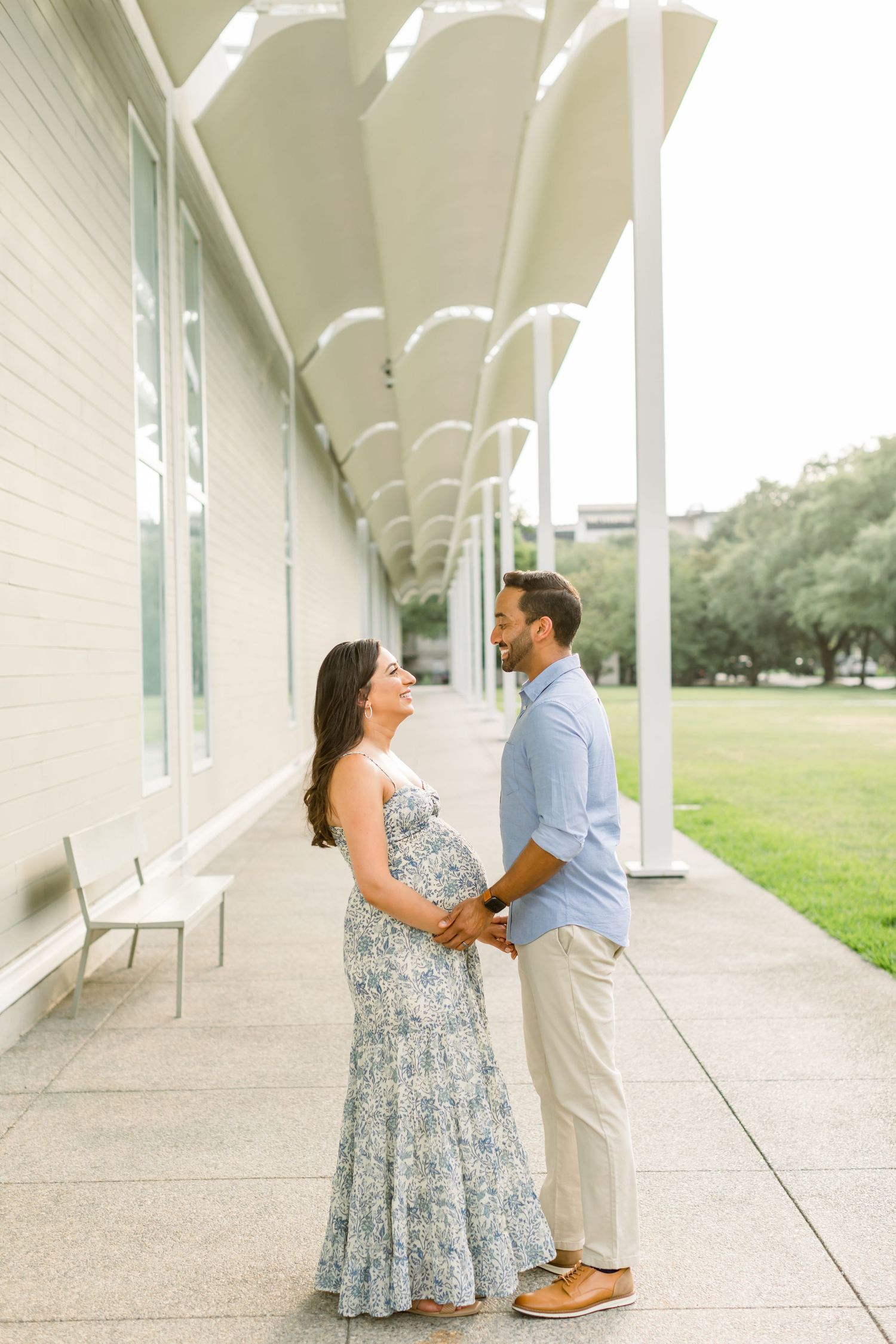 Maternity photo of couple holding hands under white columned walkway.