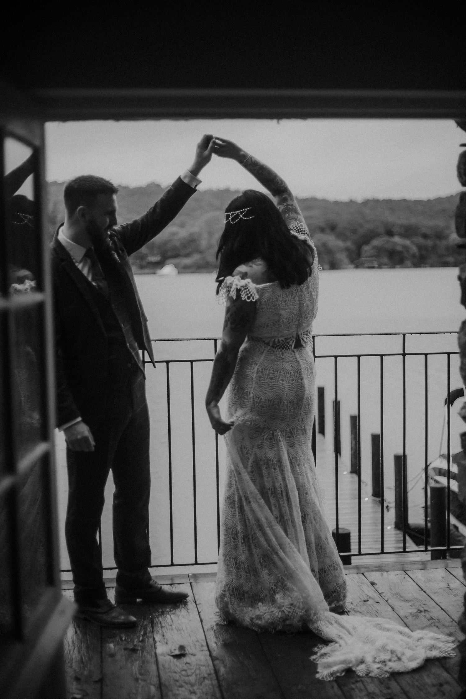 A black and white photo of a couple dancing on a waterfront deck.