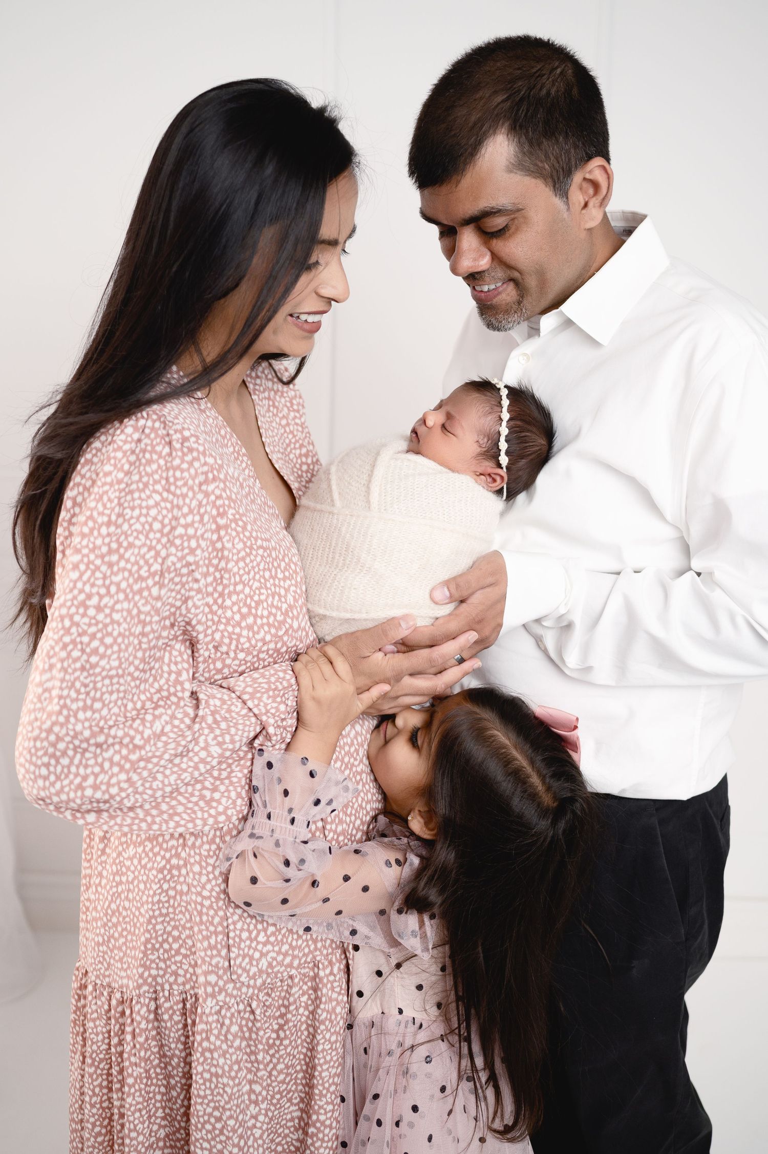 Family wearing pink and white sharing intimate moments with their newborn in studio setting.