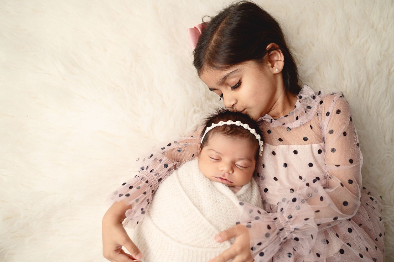 Studio portraits of siblings and newborn baby in coordinating pink outfits against white background.
