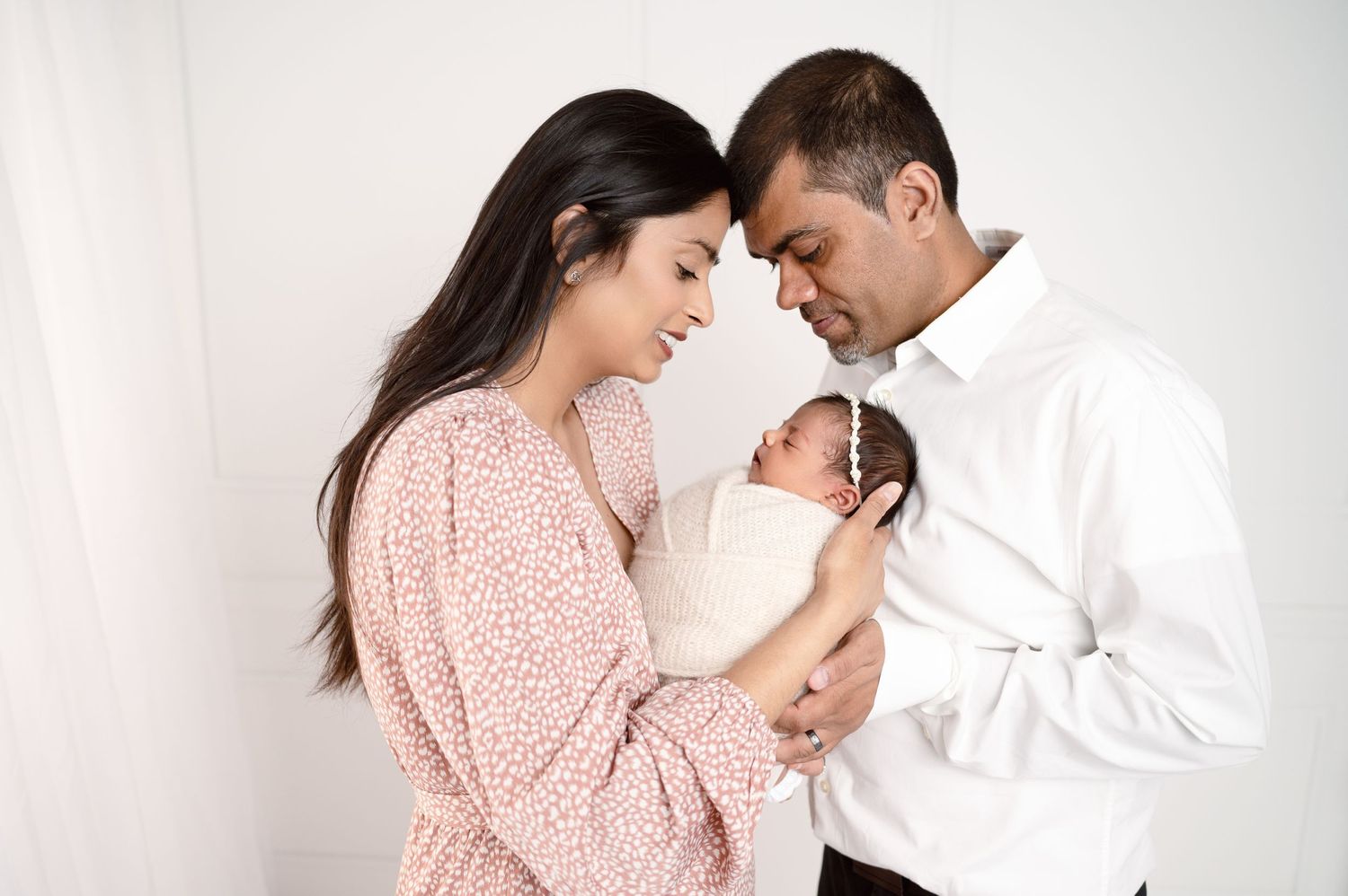 Sweet newborn photo session with parents in pink and white outfits showing tender moments with their baby.