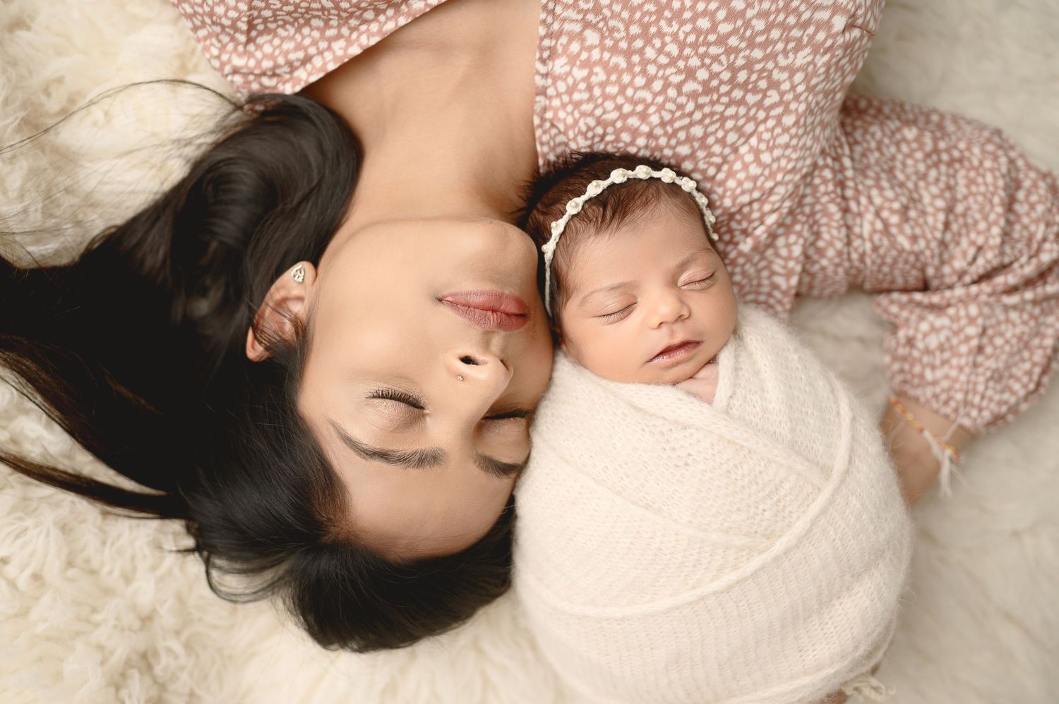 Intimate newborn photography showing parents cuddling with sleeping baby against white background.