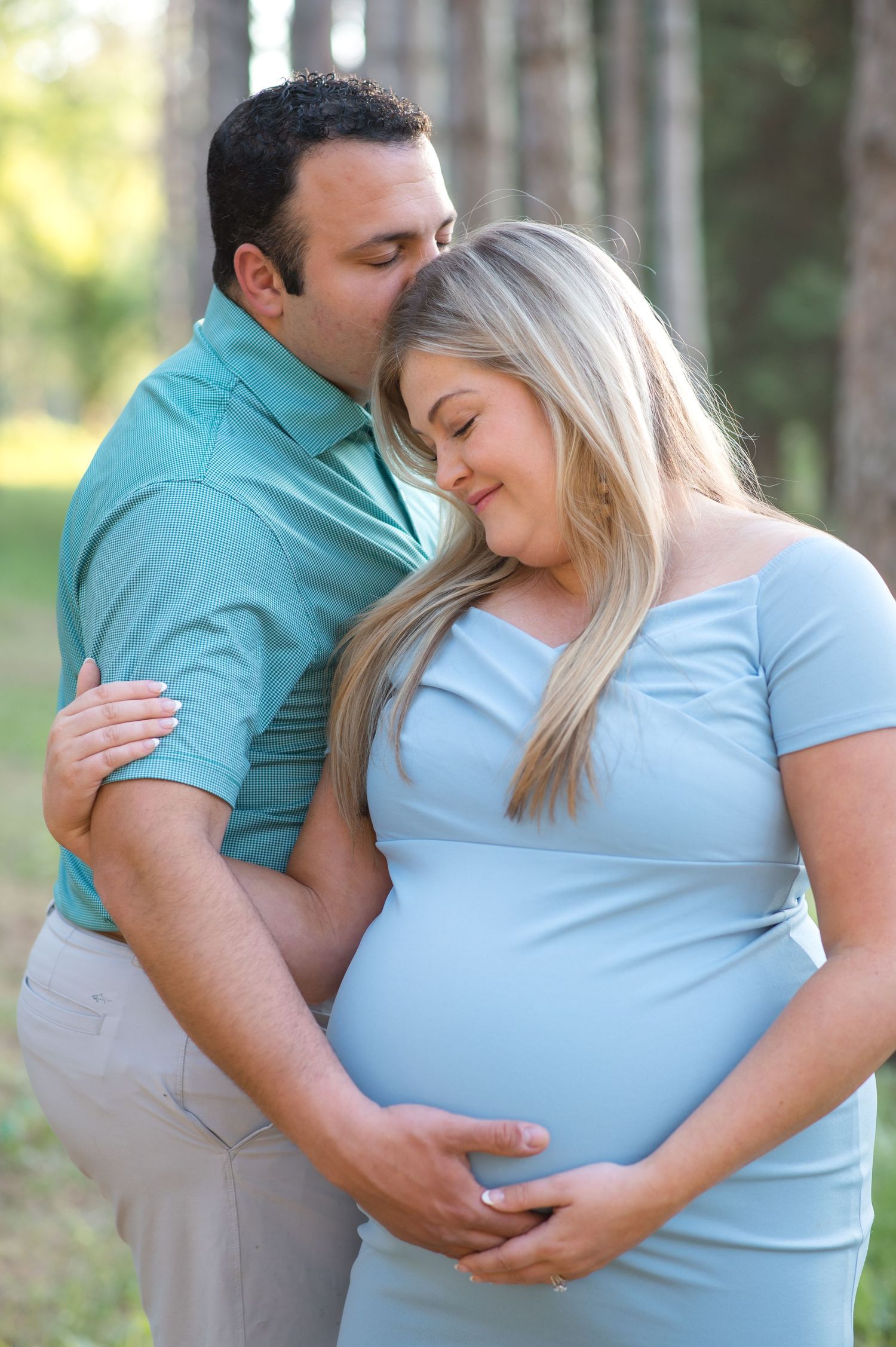 Expecting couple sharing an intimate moment outdoors in a wooded setting.