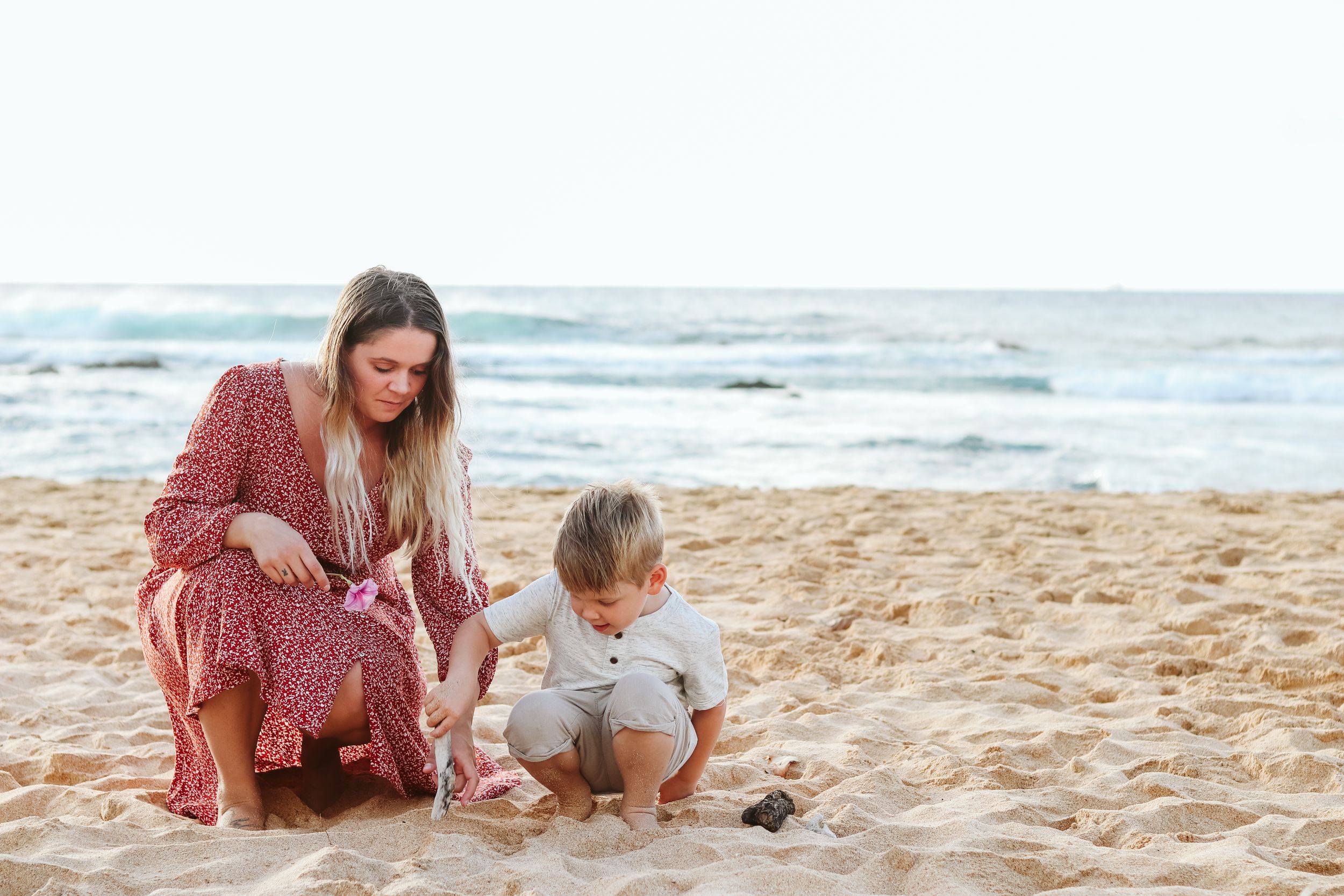 Family members explore and play in the sand at the beach on a sunny day.