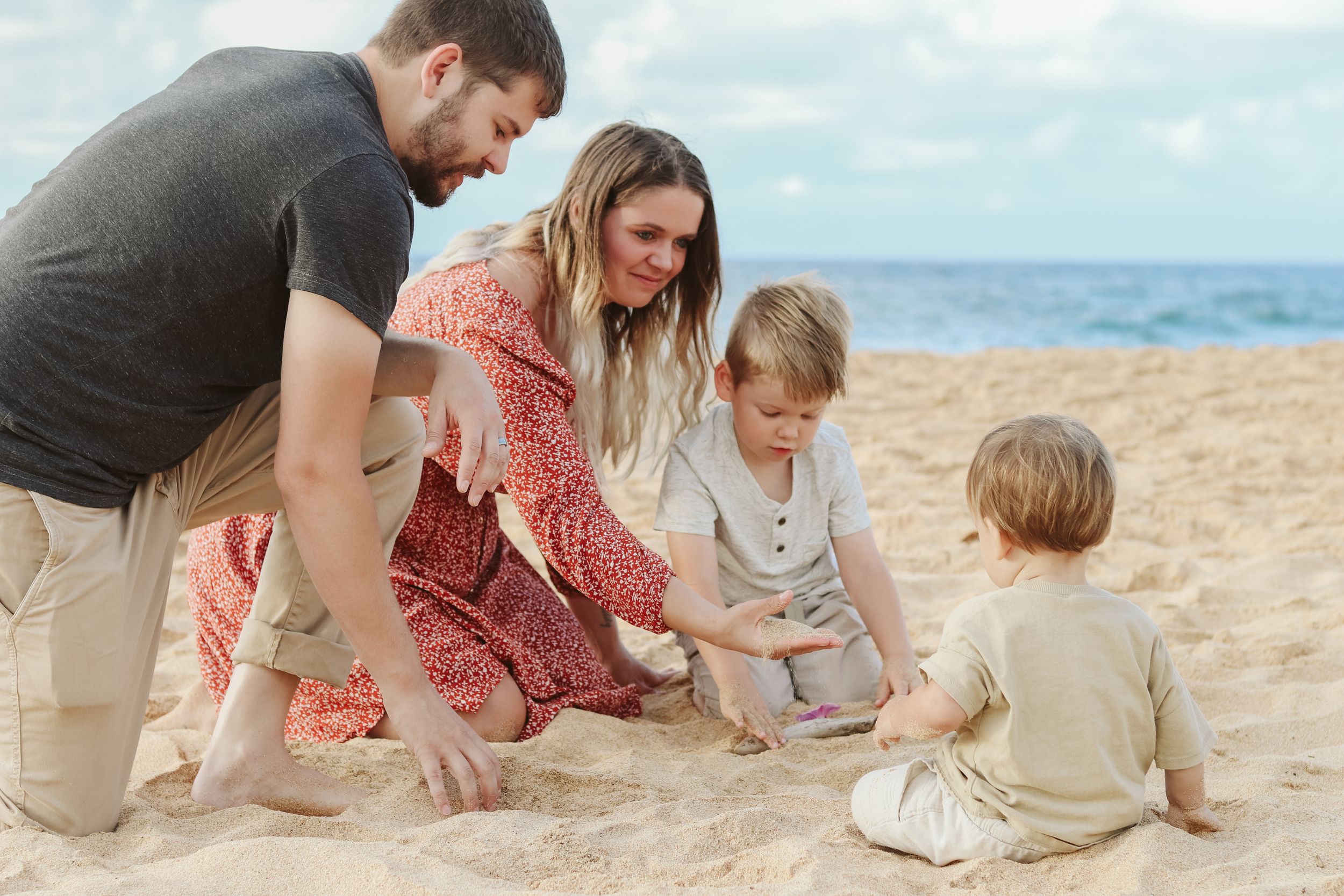 Family members interact and play together on sandy beach with ocean waves in background.