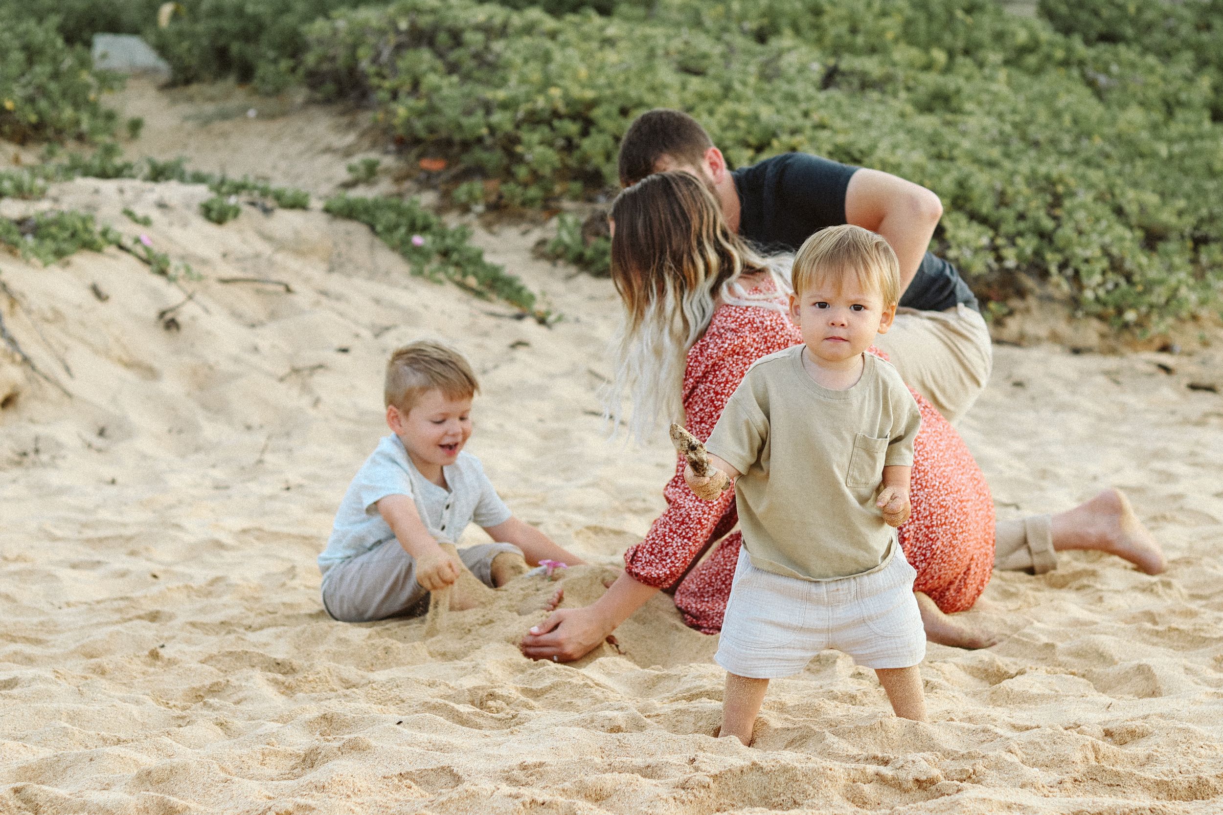 Playful family moments captured on a sandy beach with greenery in background.