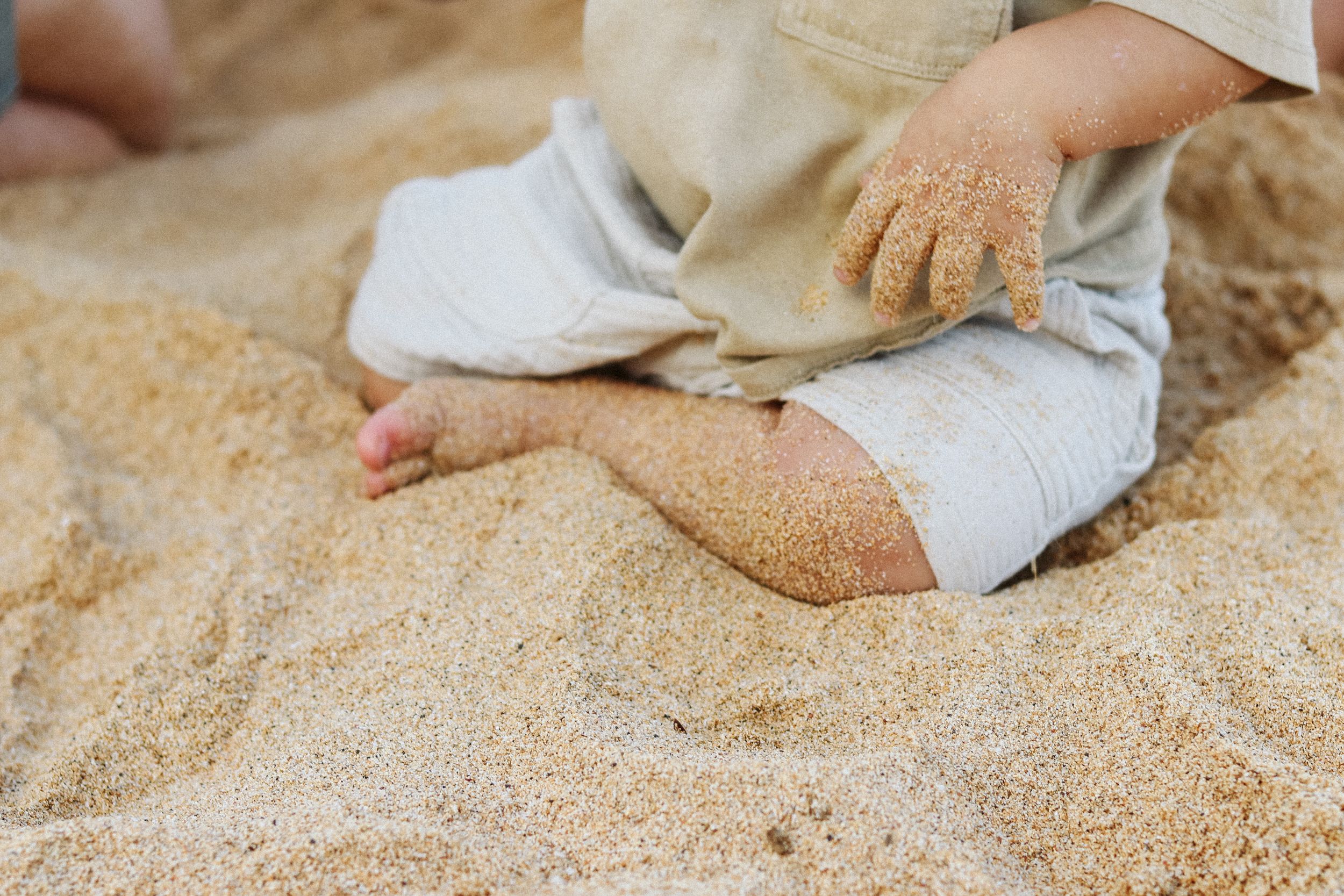 Close-up view of hands playing in golden beach sand.
