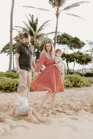 Family plays together on a tropical beach with palm trees in the background.