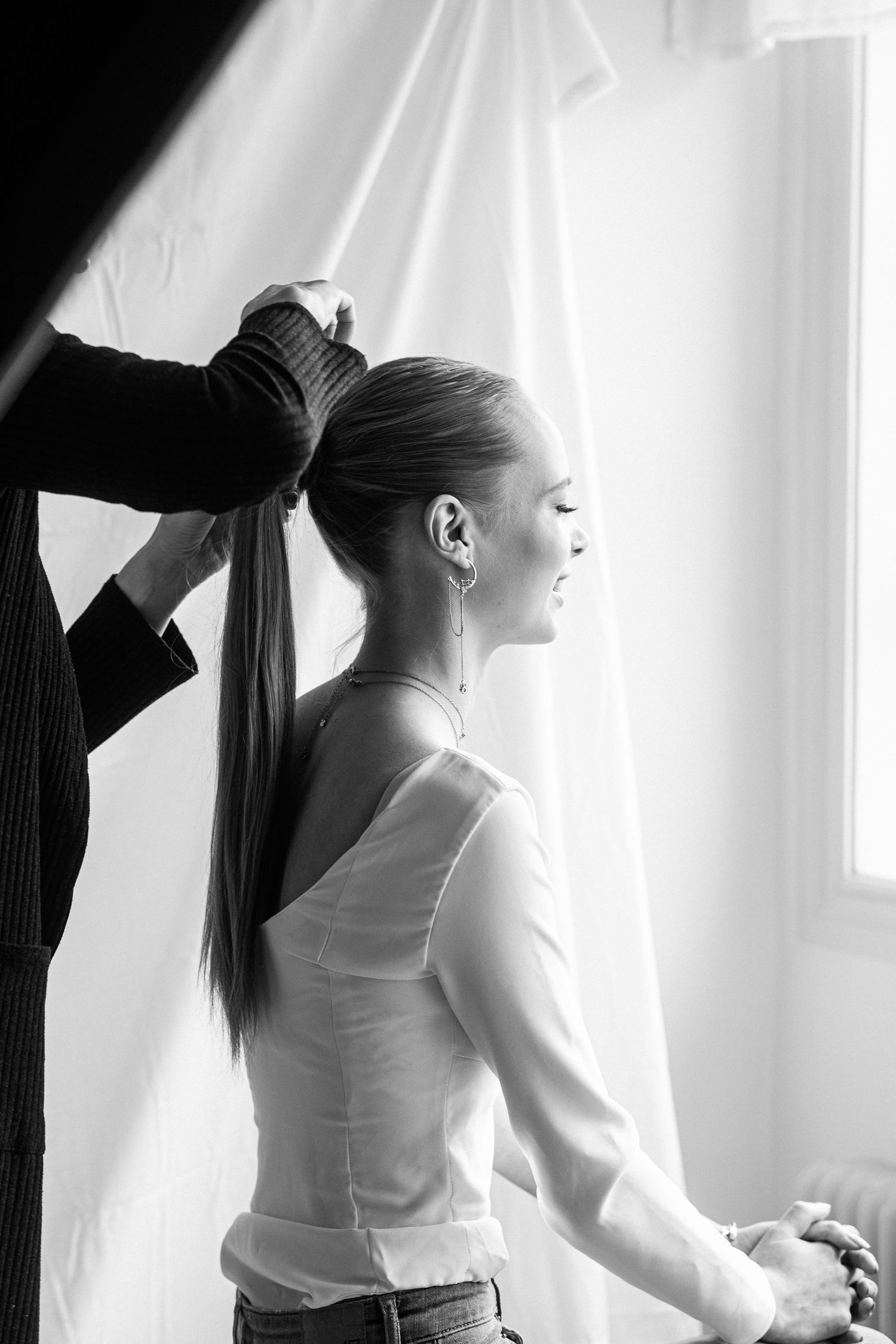 Kvinna får håret uppsatt i hästsvans vid ett fönster, bär elegant topp och smycken.
Fotograf: Gabriel Alenius, Falun