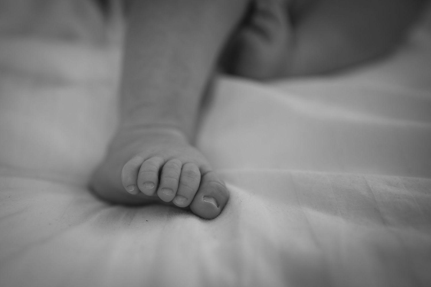 Close up black and white photo of tiny baby feet on white bedding.