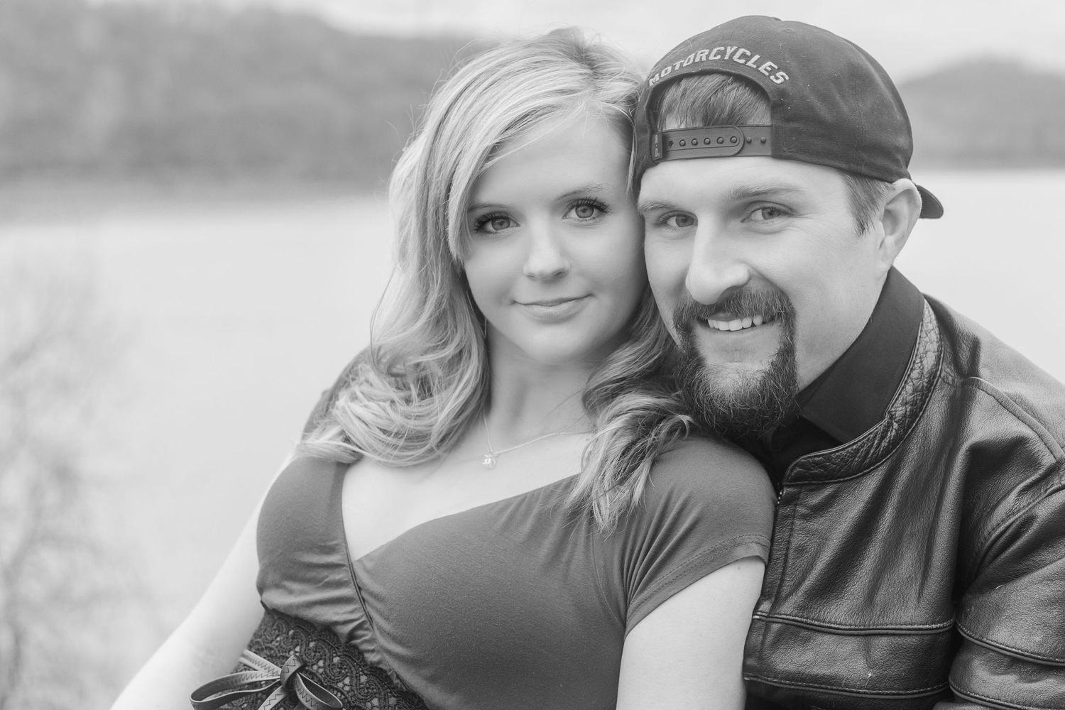 A couple smiles together during their winter lakeside photoshoot.