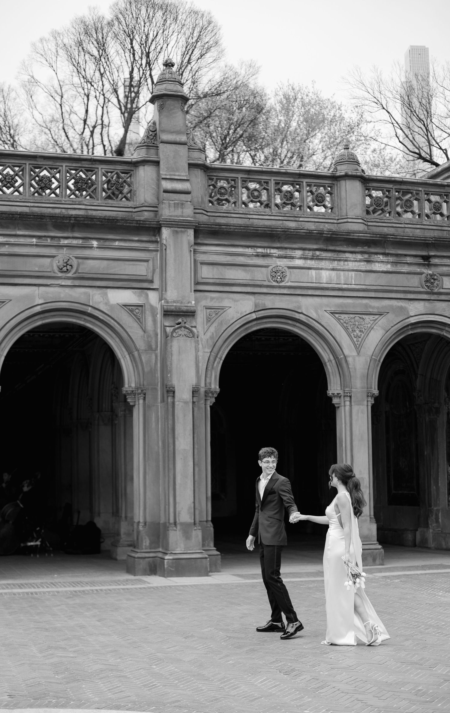 A couple walks under ornate stone archways in Central Park during their wedding photoshoot.