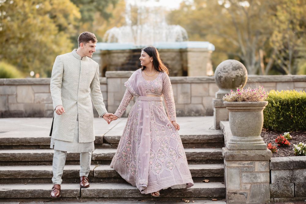 A couple in formal attire poses together on stone steps in a garden setting during golden hour.
