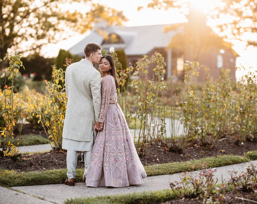 A couple shares an intimate moment against a warm sunset backdrop in a garden setting.