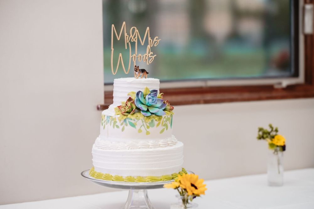 Wedding cakes decorated with gold accents and floral designs displayed on white tablecloths.