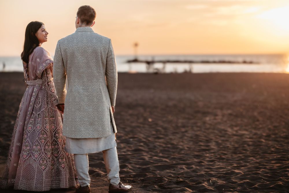 A couple stands silhouetted against a dramatic orange sunset sky.