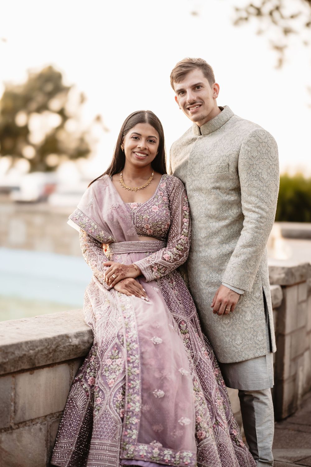 Couple in traditional fusion wedding attire with pink lehenga and cream sherwani.