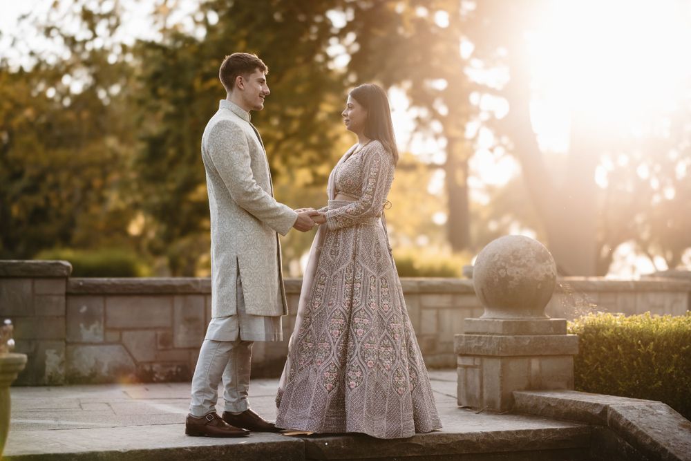 Couple in traditional Indian and Western fusion wedding outfits posing at golden hour.