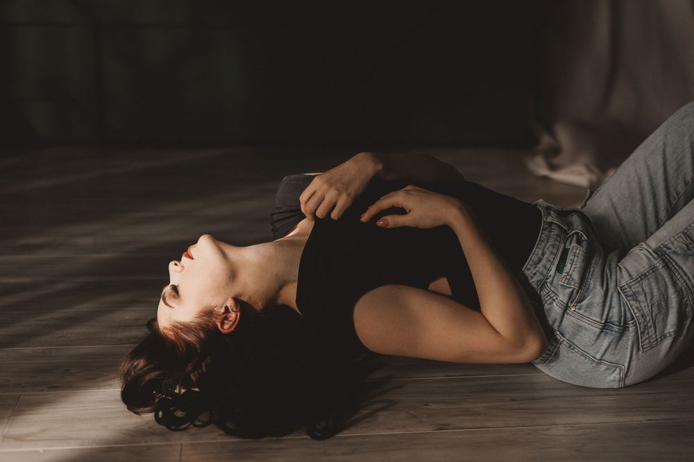 Woman laying on the ground in the sunshine, wearing a black shirt and jeans in a natural light boudoir studio