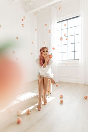 Bright summery image in a creative boudoir studio with peaches floating around a woman with pink hair, natural light