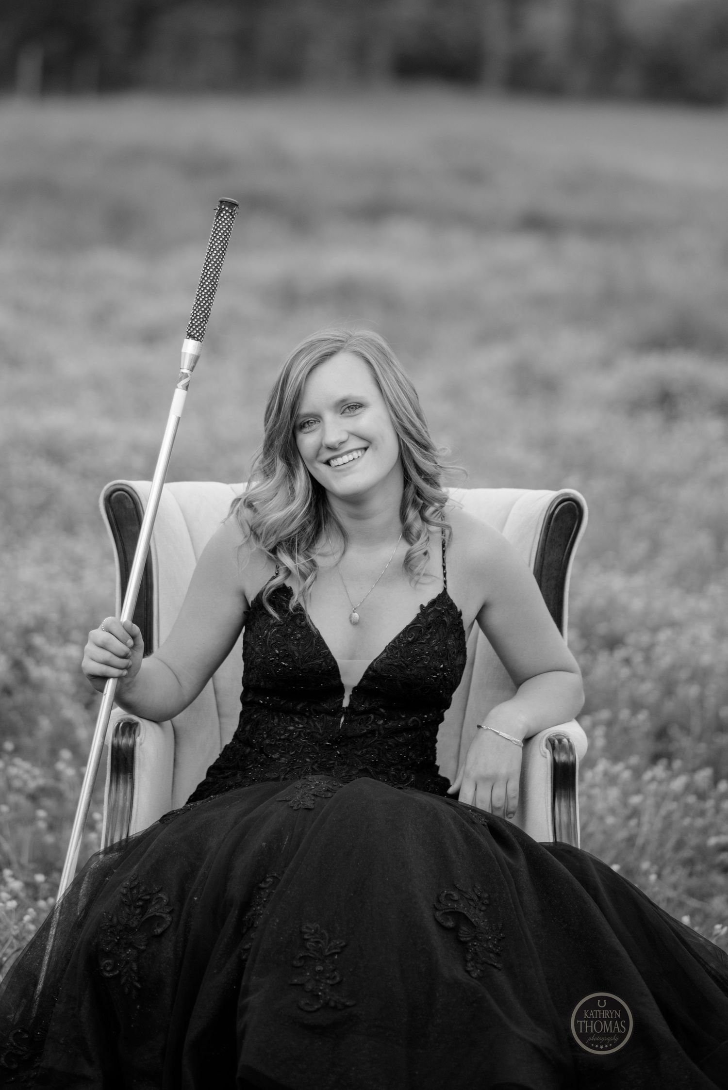 Black and white portrait of woman in formal gown holding show stick while seated in armchair.