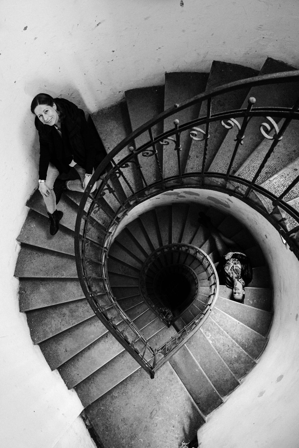 Black and white photo of two people on a spiral staircase captured from above.