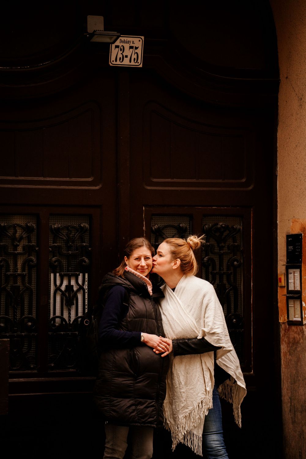 Two people sharing an intimate moment by a vintage wooden door with ornate details.