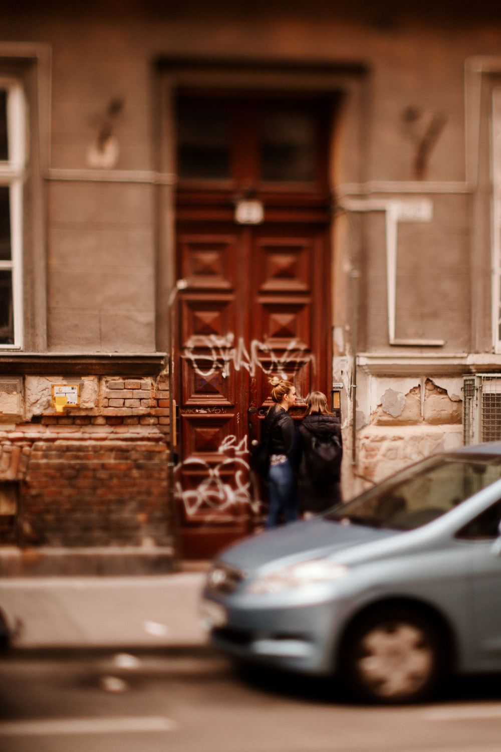 Vintage wooden door with graffiti and parked car on street.