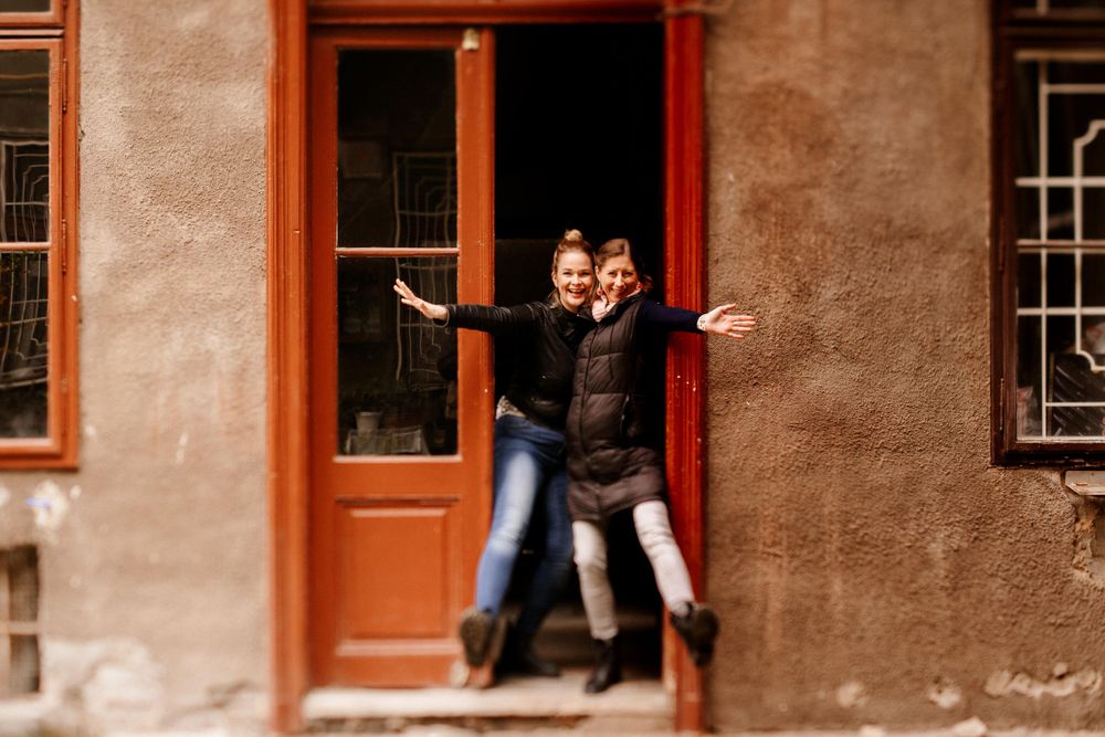 Playful pose in a red doorway of an old European building with textured walls.