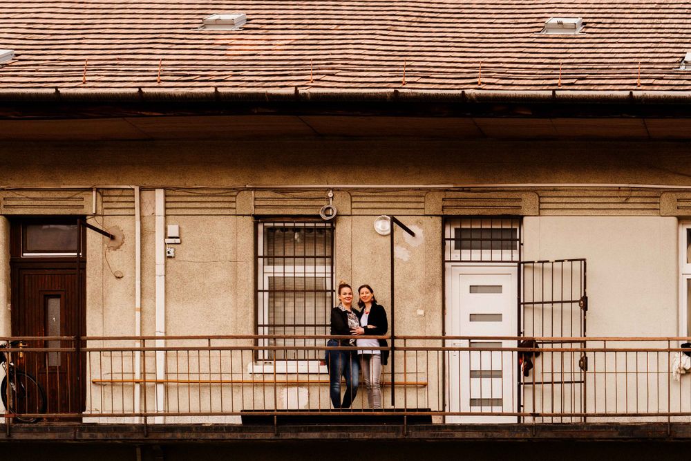 Couple standing on a vintage apartment balcony with beige facade and rustic details.