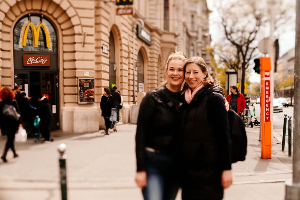 Friends pose outside historic building with McDonald's sign and urban streetscape.