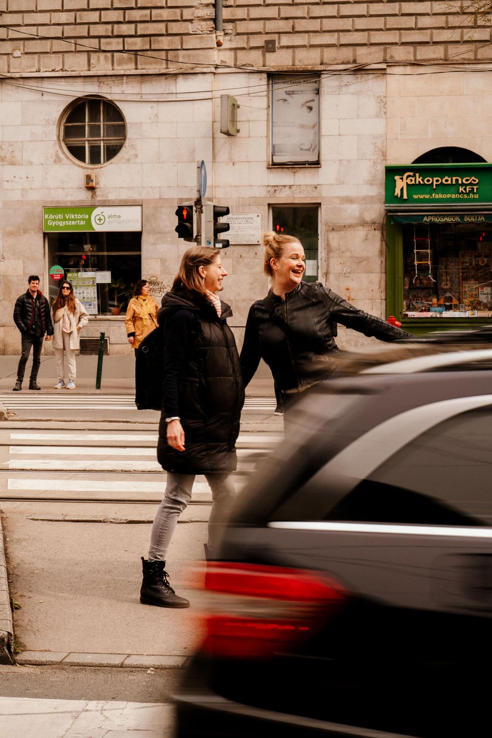 Two friends crossing city street with motion blur of passing car.