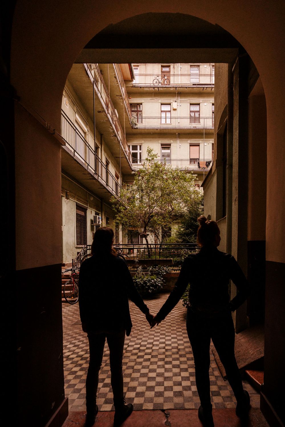 Silhouettes of two people holding hands while standing in an arched passageway.