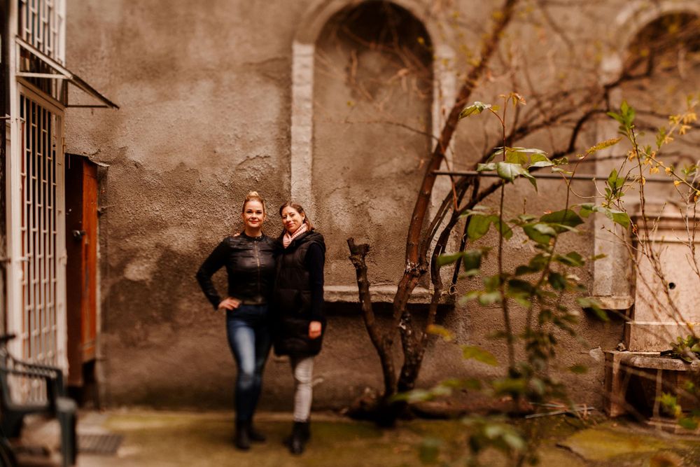Two people walking together near old stone wall with bare branches.