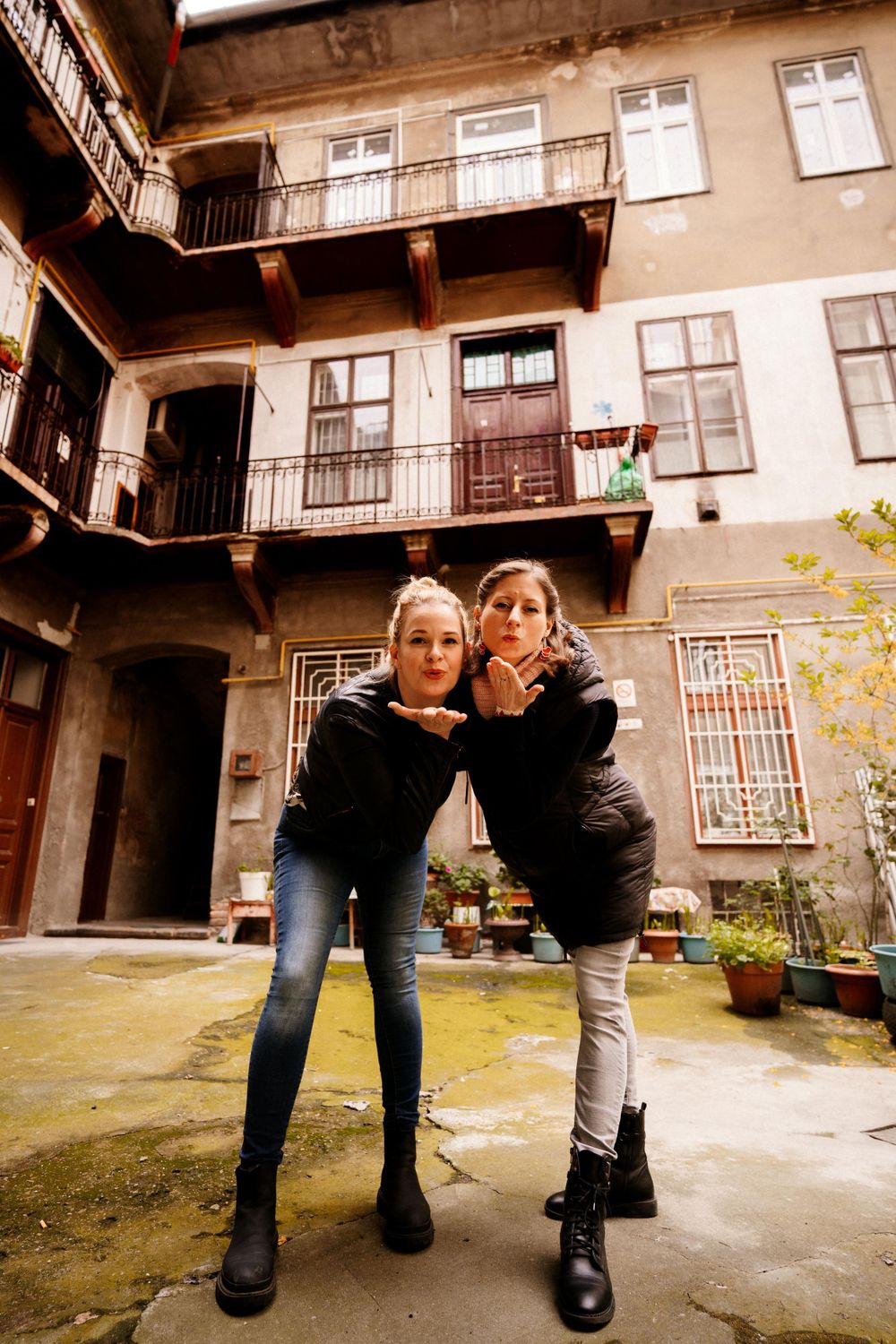 Two friends posing playfully in a rustic courtyard with old balconies and stone walls.