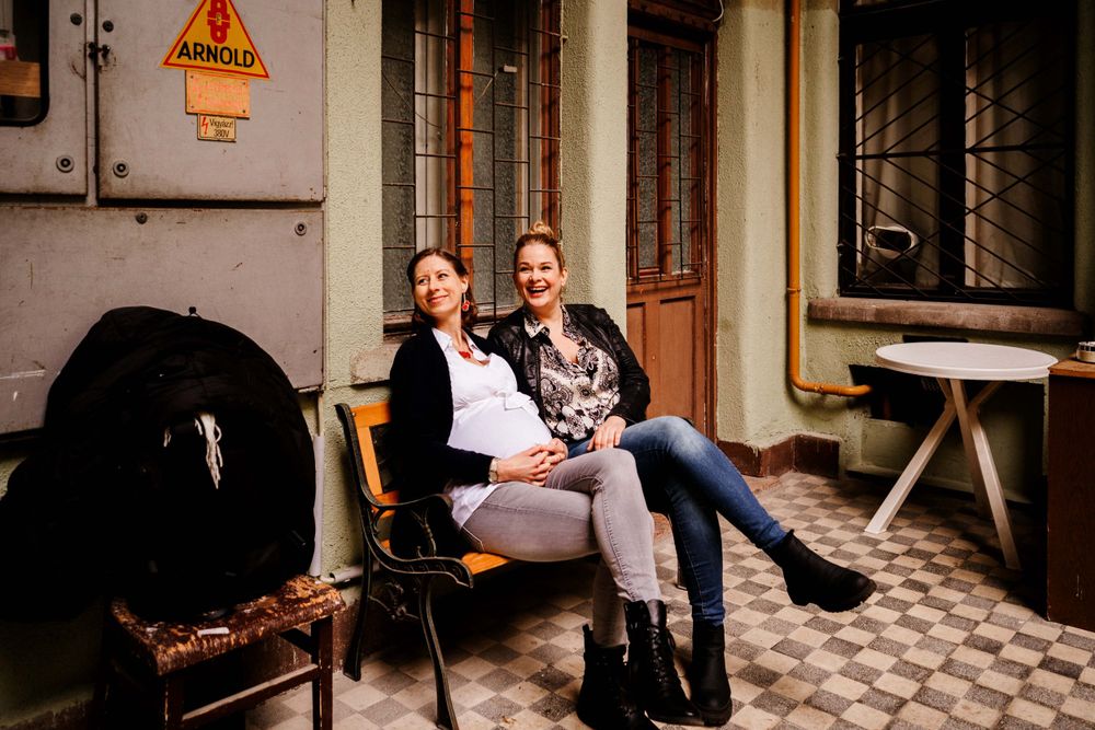Two people sitting together on a bench in front of a vintage building with checkered floors.