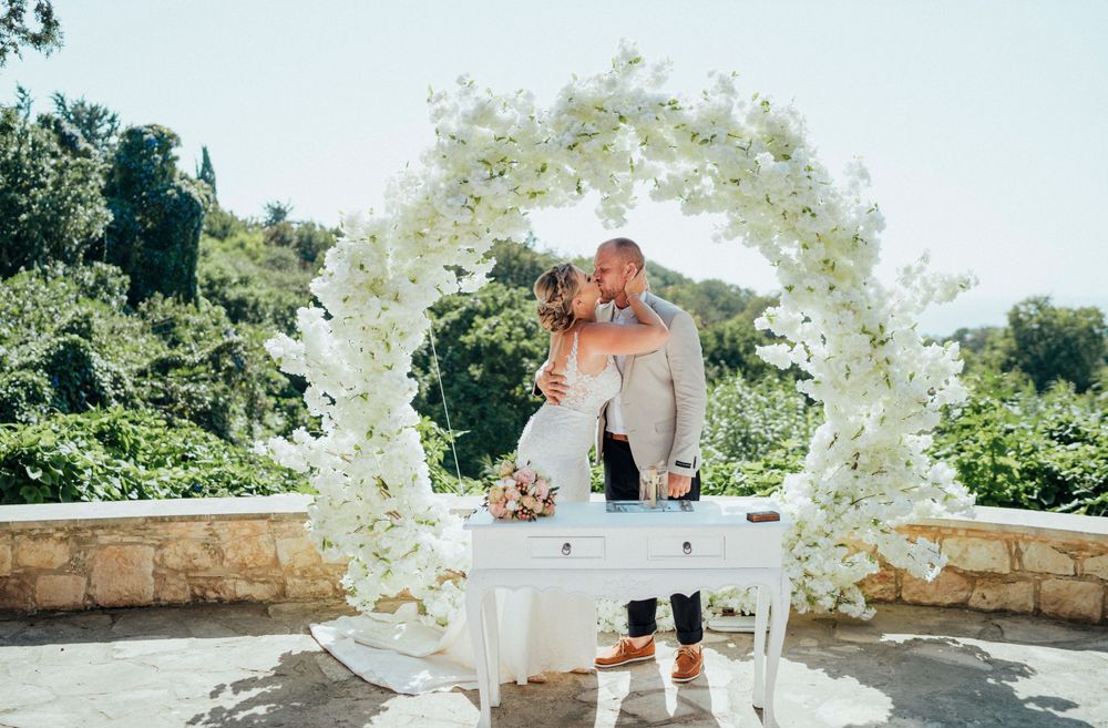 Wedding ceremony setup with white floral arch in garden setting.