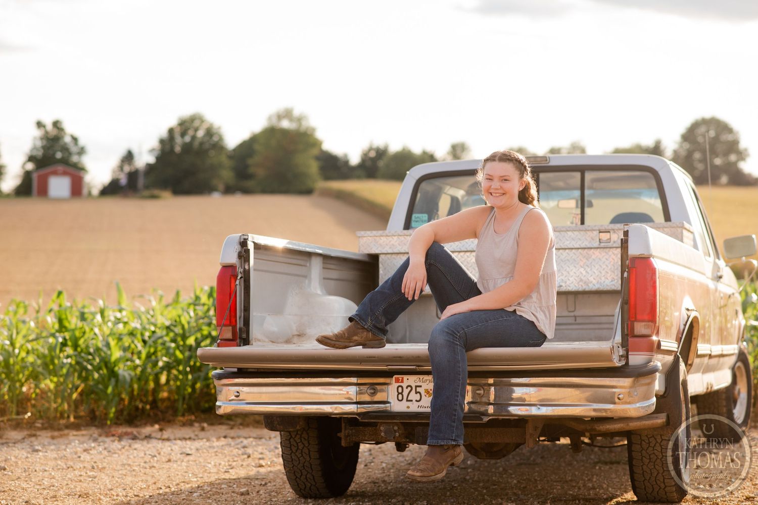 Golden hour portrait with person sitting in bed of vintage pickup truck by cornfield.