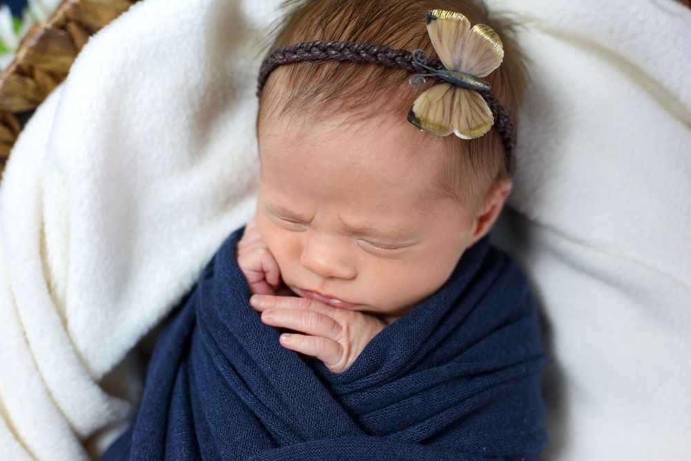 Newborn baby girls rests soundly with butterfly resting on her head during newborn studio photography session.