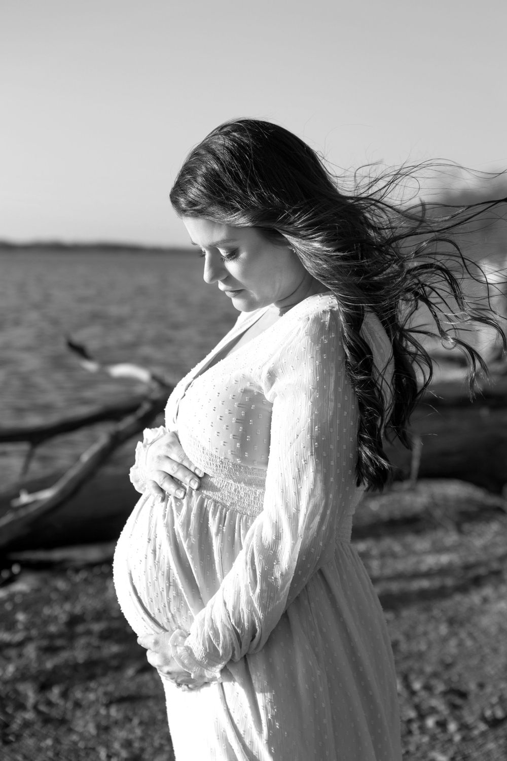 Pregnant mother looking at her belly bump as the wind blows her hair.