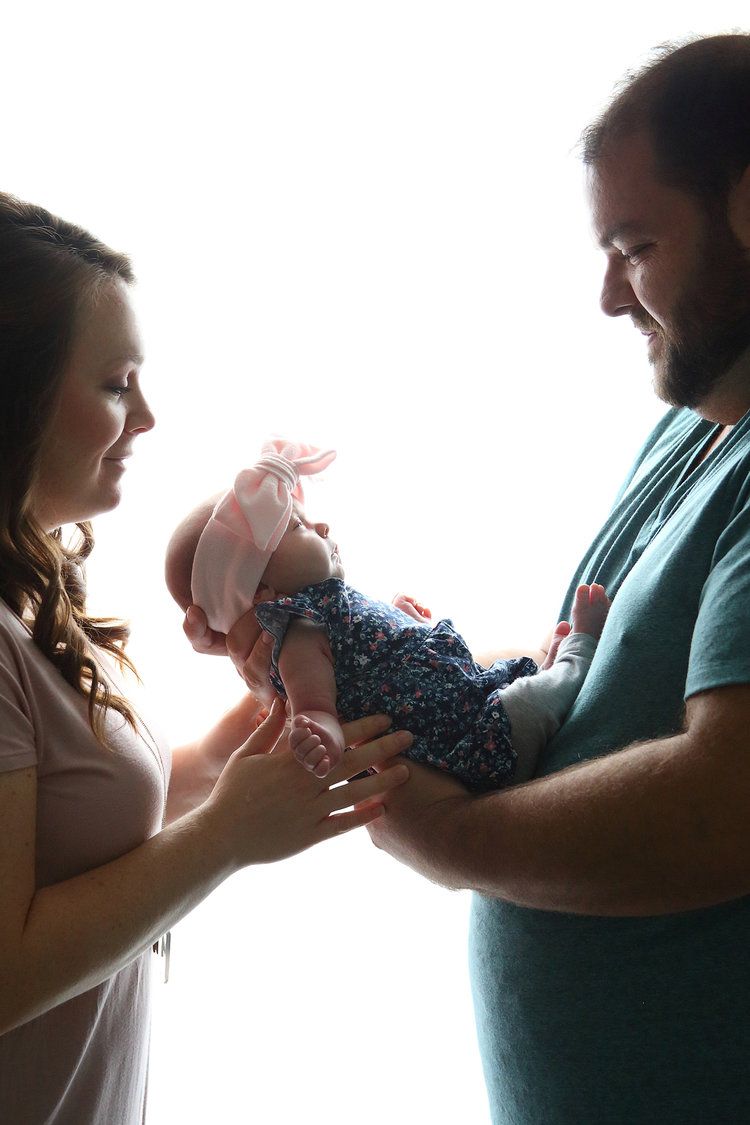 Newborn baby is cradled in parents arms during their in home photography session.